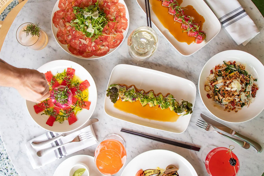 An outdoor dining table with beautifully plated dishes and cocktails